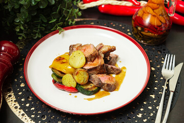 Grilled steak with roasted vegetables and sauce. Juicy sliced grilled steak served with roasted zucchini, potatoes, bell peppers, and savory brown sauce on a white plate.