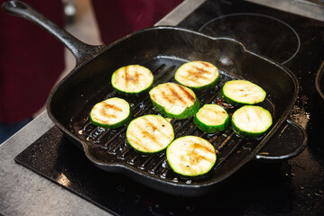 Grilling zucchini slices on a stovetop pan. Sliced zucchini cooking on a hot grill pan, showing sear marks and steam rising during stovetop vegetable preparation.