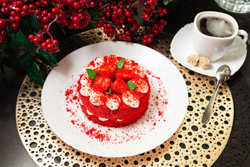 Red velvet strawberry cake with coffee cup. Bright red velvet cake topped with strawberries and cream, served with a hot black coffee and sugar cubes on the side.