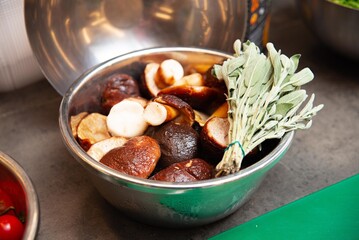 Fresh Sage and Mixed Mushrooms in Metal Bowl. A stainless steel bowl filled with a variety of mushrooms and a bundle of fresh sage, ready for cooking preparation.
