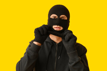 Male thief putting on balaclava on yellow background