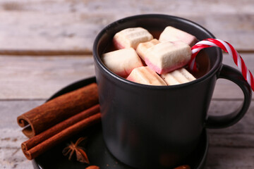 Cup of hot chocolate with marshmallows, candy cane and different spices on grey wooden background