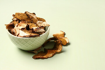 Bowl with tasty dried mushrooms on green background