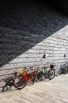 Row of bicycles aligned along brick wall with strong diagonal shadow. Urban design elements and Copenhagen street textures captured with precision.
