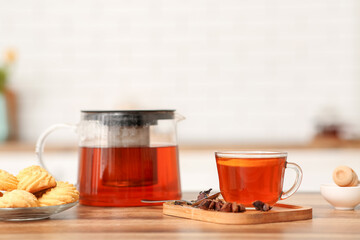 Teapot and cup of black tea with cookies on table in kitchen
