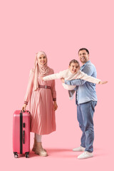 Beautiful Muslim family with suitcase on pink background. Travel concept