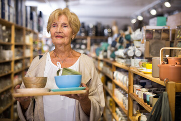Senior woman customer holding purchases and walking in a household goods store