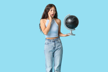 Fototapeta premium Surprised young Asian woman with globe on blue background. Travel concept