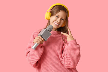 Cute girl in headphones with modern microphone showing victory gesture on pink background