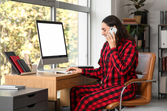 Young businesswoman talking by mobile phone at table in office. National Wear Your Pajamas to Work Day