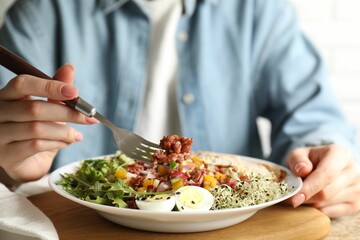 Woman eating delicious salad with brown rice at wooden table, closeup