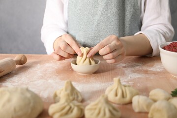 Woman making khinkali on table in kitchen, closeup