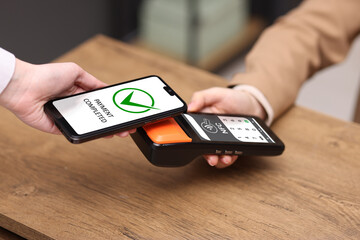 Payment terminal with NFC system. Client using mobile phone to pay for service indoors, closeup
