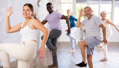 Dynamic young instructor and mature attendees of dancing courses training Rock and Roll dance poses in dancehall