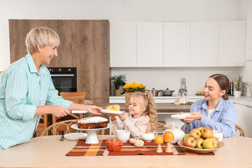 Mature woman giving piece of pie to her granddaughter in kitchen