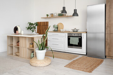 Fototapeta na wymiar Interior of stylish kitchen with island table, houseplants and modern refrigerator