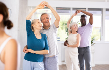 Dynamic mature attendees of dancing courses training poses of Waltz in dance hall