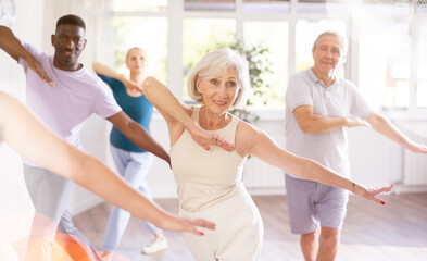 Fototapeta premium Enthusiastic elderly woman practicing modern vigorous dance movements in group dance class for adults
