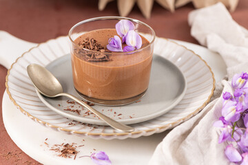A single serving of creamy chocolate mousse in a glass, elegantly garnished with purple flowers and chocolate shavings, styled on a plate.