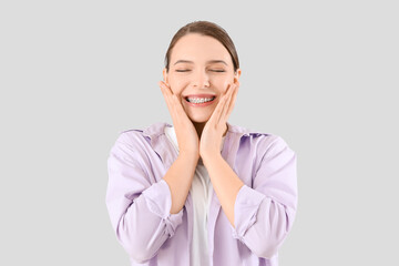 Happy young woman with dental braces smiling on light background
