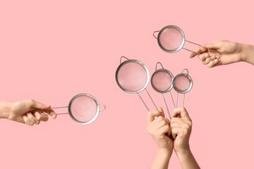 Female hands with sieves on pink background