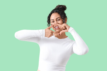 Smiling young African-American woman making frame gesture on green background
