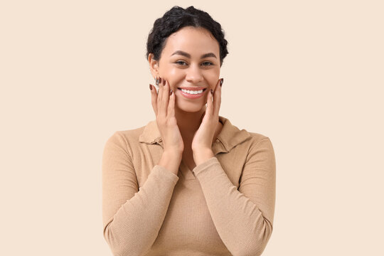 Smiling young African-American woman with healthy teeth on beige background