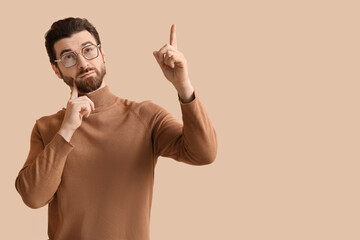 Thoughtful young man pointing up on beige background