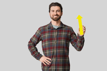 Young man with arrow pointing up on light background