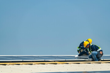 Fototapeta premium Two engineers install solar panels on a rooftop, wearing safety gear and helmets. The scene showcases renewable energy, green technology, and sustainable solutions under a clear blue sky.