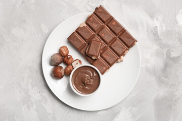 Bowl of sweet chocolate spread and hazelnuts on grey background