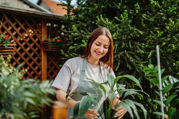 Young woman taking care of plants with water can and mister	
