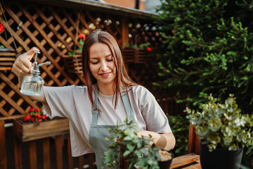 Young woman taking care of plants with water can and mister	
