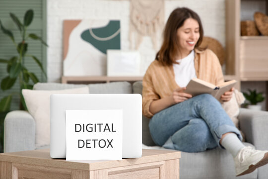 Paper with text DIGITAL DETOX and laptop on table against woman reading book at home. National Day of Unplugging