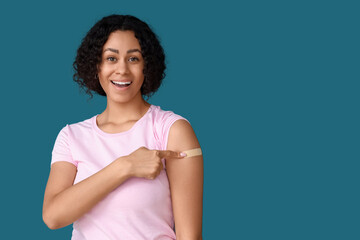 Young African-American woman pointing at applied medical patch after vaccination on blue background