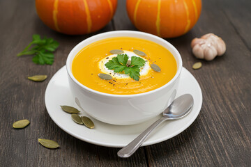 Pumpkin soup with cream and pumpkin seeds in white bowl on wooden table