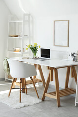 Interior of light office with workplace, flowers and shelf unit