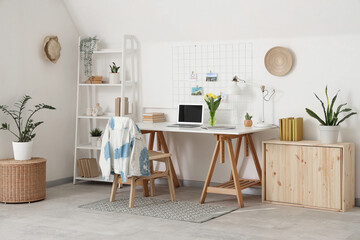 Interior of light office with workplace, flowers and shelf unit