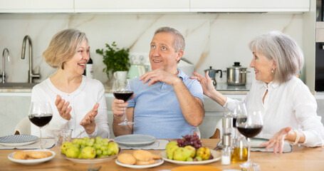 Happy pensioners gathered at the festive table - talking, discussing news and drinking red wine