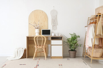 Interior of office with workplace, blossoming branches in vase and clothes rack