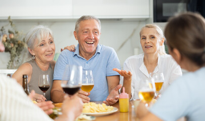 Group of happy seniors celebrating holiday drinking and chatting at table at home