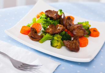 Appetizing braised chicken hearts with vegetable garnish of steamed broccoli and carrots..