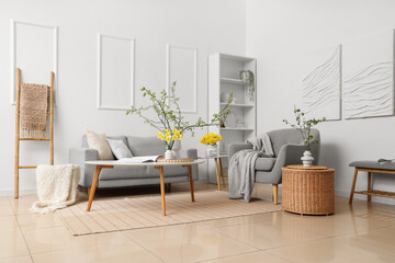 Interior of living room with grey sofa, daffodils and blossoming branches in vases