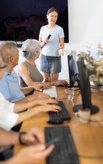 Enthusiastic female tutor teaching group of seniors in computer workshop, promoting technology...