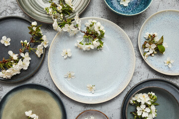 Different clean plates with blooming branches on grey background