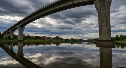 Bridge over water reflecting sky symbolizing connection and infrastructure, with cloudy sky