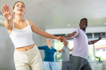 Young woman coach rehearsing with group of multinational sports aged people social dance in dance...
