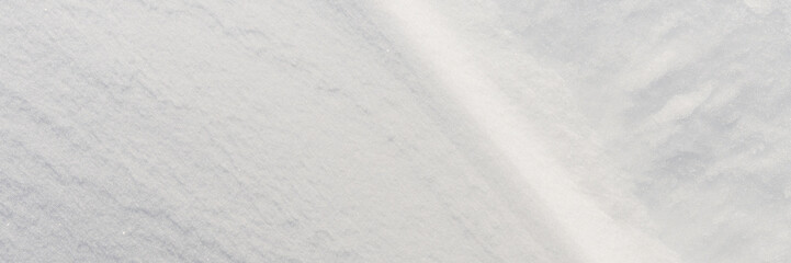 Beautiful winter background with snowy ground. Natural snow texture. Wind sculpted patterns on snow surface. Wide panoramic texture for background and design. Closeup top view with copy space.