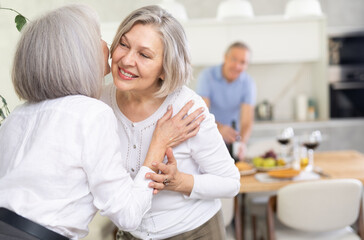 Obraz premium Two elderly women friends hugging in kitchen at home