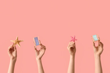 Female hands holding mini deck chairs with starfishes on pink background